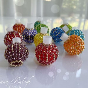 Op de afbeelding: Een verzameling bolvormige kralenornamenten in diverse kleuren, waaronder rood, paars, geel, blauw, groen en oranje. Elk ornament is voorzien van een kleine witte cilindrische plastic bovenkant en is gemaakt met glaskralen en gouden accenten.