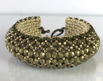 May include: A beaded bracelet with a gradient of green and gold beads. The bracelet is made with small, faceted beads and has a simple, elegant design.