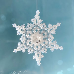 May include: A white beaded snowflake ornament hanging from a string against a light blue background.