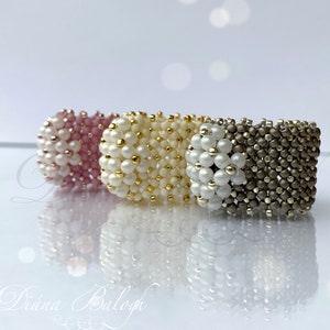 May include: Three beaded rings in pink, white and gold, and gray. The rings are stacked on top of each other.