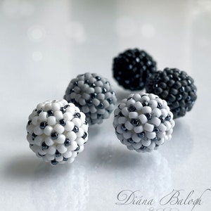 Puede incluir: Cinco pequeños adornos redondos de cuentas en tonos grises y blancos. Los adornos están hechos de pequeñas cuentas que se cosen juntas para crear una forma esférica. Los adornos están dispuestos en un grupo sobre una superficie blanca.