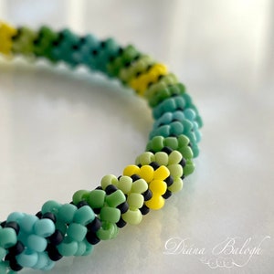 Puede incluir: Primer plano de una pulsera de cuentas con un degradado de cuentas azules, verdes y amarillas. Las cuentas están dispuestas en espiral.