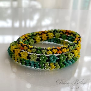 Peut inclure: Trois bracelets perlés aux tons de jaune, vert, orange et noir. Les bracelets sont faits de petites perles rondes disposées en motif floral. Les bracelets sont empilés les uns sur les autres, créant un effet de superposition. Les bracelets sont sur une surface blanche.