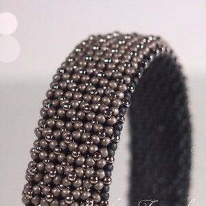 May include: A close-up of a beaded bracelet with a black elastic band. The bracelet is made with small, round beads in shades of brown and silver.