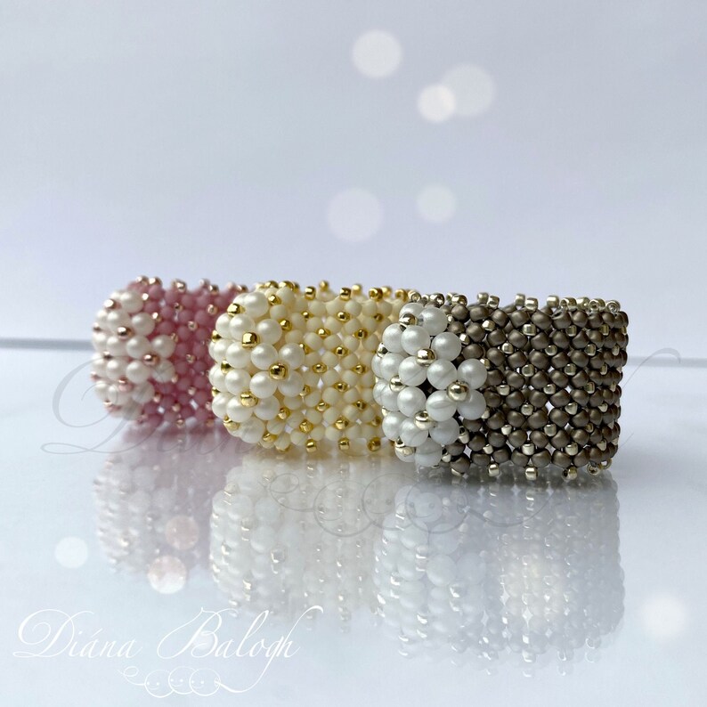 May include: Three beaded rings in pink, white and gold, and gray. The rings are stacked on top of each other.