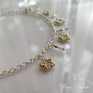 May include: A silver chain necklace with multiple gold star-shaped charms and clear crystal beads hanging from it.