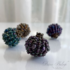 May include: Four small, iridescent, beaded spheres in shades of teal, brown, purple, and green. The spheres are made of tiny beads and have a textured, organic look.