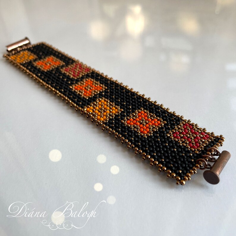 Puede incluir: Un brazalete de cuentas negras con detalles en naranja, rojo y dorado. El brazalete tiene un patr&oacute;n geom&eacute;trico y se asegura con un cierre de metal.