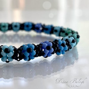 May include: A close-up of a beaded bracelet with a gradient of blue and black beads. The beads are arranged in a flower pattern.