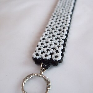 May include: A black and white beaded keychain with a silver ring. The beads are arranged in a geometric pattern.