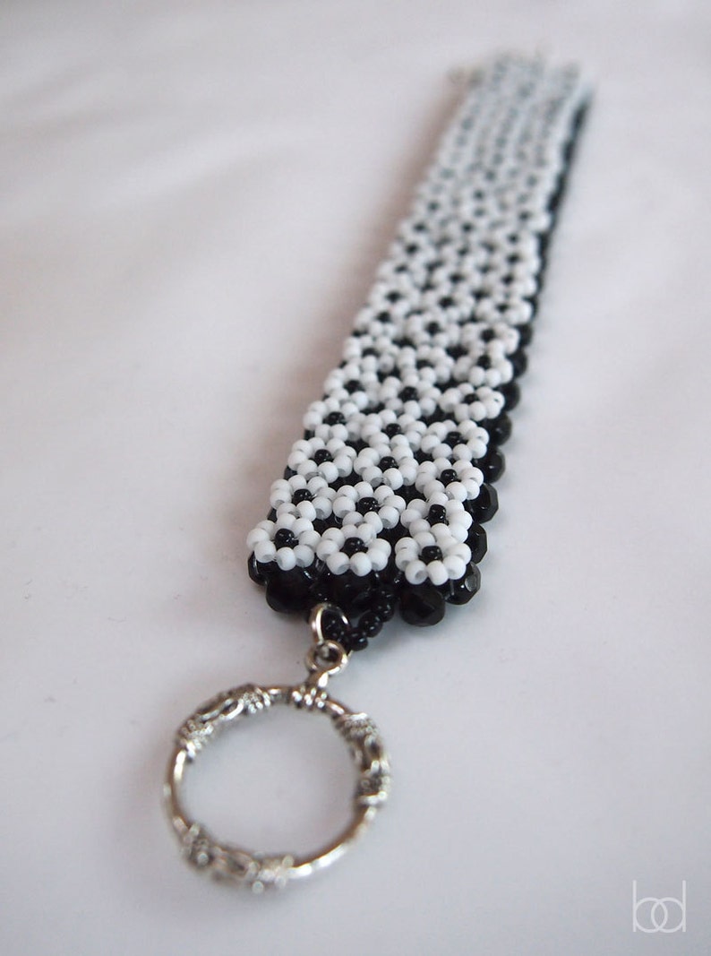 May include: A black and white beaded keychain with a silver ring. The beads are arranged in a geometric pattern.
