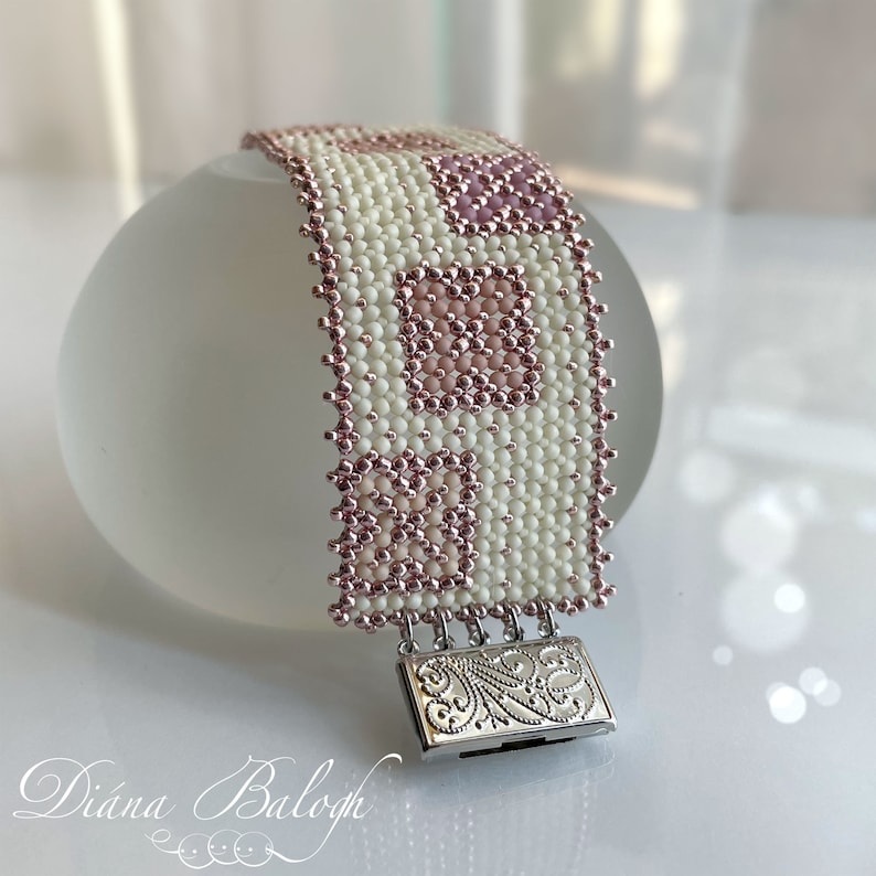 Puede incluir: Un brazalete de cuentas blancas y rosas con un cierre plateado. El brazalete tiene un patr&oacute;n geom&eacute;trico con cuadrados y rect&aacute;ngulos.