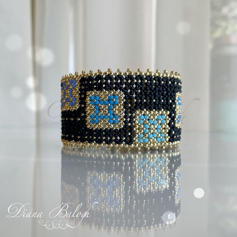 Puede incluir: Un brazalete de cuentas negras con patrones geom&eacute;tricos dorados y azules. El brazalete est&aacute; hecho con cuentas peque&ntilde;as y tiene una superficie texturizada.