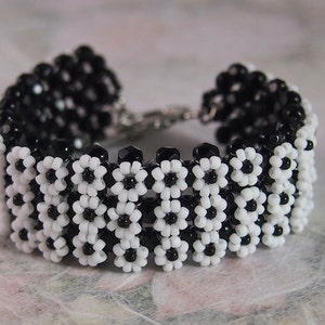 May include: A black and white beaded bracelet featuring a flower design. The bracelet is crafted from small, round beads that are strung together to create a pattern of flowers.