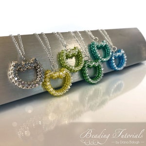 May include: Five beaded heart necklaces in different colors, including silver, yellow, green, blue, and turquoise. The necklaces are on a silver surface. The image includes the text "Beading Tutorials - by Diana Balogh - "