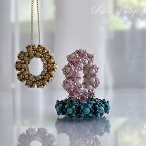 Puede incluir: Tres anillos de cuentas, uno en beige, uno en rosa y blanco, y uno en turquesa y azul oscuro. Los anillos están apilados uno encima del otro.