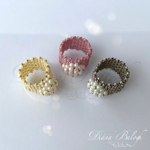 May include: Three beaded rings with a white pearl center. The rings are made with pink, cream, and gray beads.