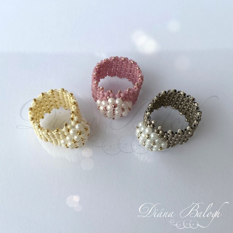 May include: Three beaded rings with a white pearl center. The rings are made with pink, cream, and gray beads.