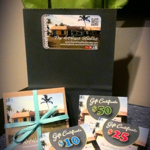 May include: Four gift certificates for The ArtHaus Studios, with values of $10, $25, $50, and $100. The certificates feature a tropical scene with a blue sky, palm trees, and a yellow building.