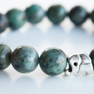 May include: A green gemstone bracelet with a silver elephant charm. The bracelet is made of round beads and has a simple design.