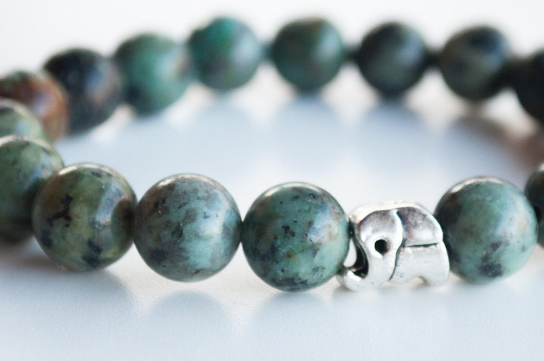 May include: A green gemstone bracelet with a silver elephant charm. The bracelet is made of round beads and has a simple design.