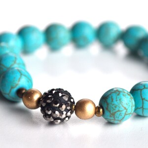 May include: Turquoise and gold beaded bracelet with a black rhinestone accent bead.