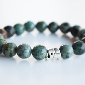 May include: A turquoise green beaded bracelet with a silver elephant charm.