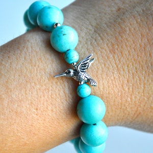 Op de afbeelding: Turquoise kralen armband met een zilveren kolibrie bedel. De armband is gemaakt van ronde kralen en heeft een eenvoudig ontwerp.