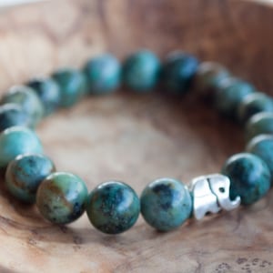 May include: A turquoise gemstone bracelet with a silver elephant charm. The bracelet is made of round beads and is strung on an elastic cord.