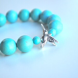 Op de afbeelding: Turquoise kralen armband met een zilveren kolibrie bedel.