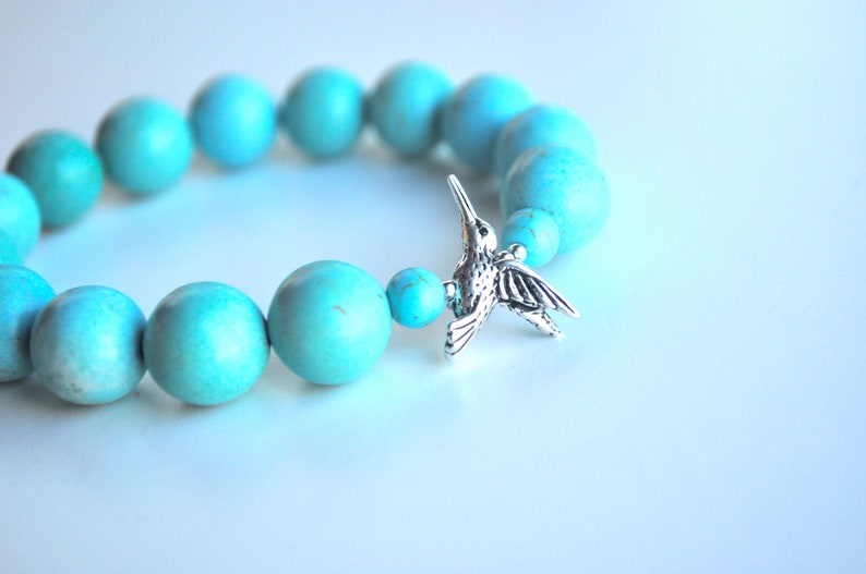 Op de afbeelding: Turquoise kralen armband met een zilveren kolibrie bedel.