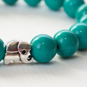 May include: A turquoise beaded bracelet with a silver elephant charm. The beads are round and smooth, and the charm is detailed and intricate.
