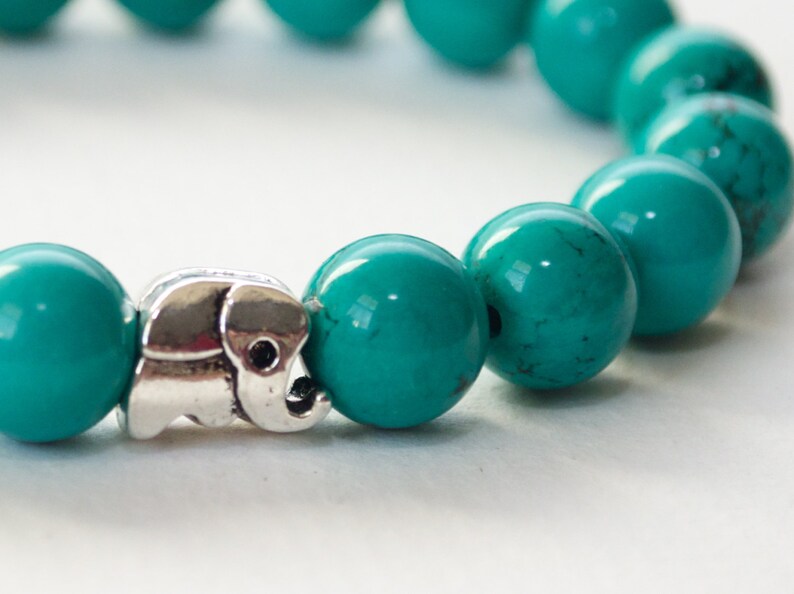 May include: A turquoise beaded bracelet with a silver elephant charm. The beads are round and smooth, and the charm is detailed and intricate.