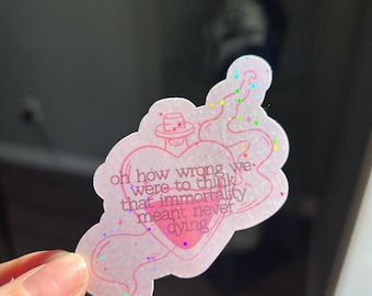 May include: A pink sticker with a heart and bottle design, featuring the text "oh how wrong we were to think that immortality meant never dying." The sticker has a glittery, iridescent finish and is held by a hand.