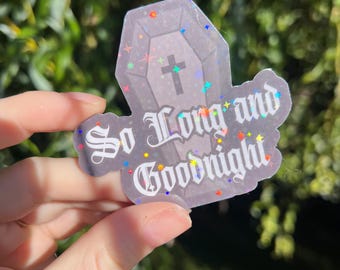 May include: A coffin-shaped sticker with the text "So Long and Goodnight" in a gothic font. The sticker has a gray coffin design with a cross and is decorated with colorful star-shaped glitter.