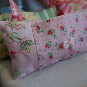 May include: A pink and white floral fabric eye pillow with a pink satin bow. The pillow is filled with a soft material and is designed to help block out light and promote relaxation.