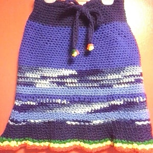 May include: A crocheted skirt with a blue, purple, and white striped pattern. The skirt has a dark blue waistband with a drawstring and a yellow, green, and orange ruffled hem.