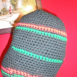 May include: A black crocheted beanie with red and green stripes. The beanie is made of a soft, textured yarn.