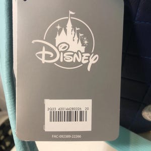 May include: A gray tag with the Disney logo, featuring a castle silhouette. Below the logo is a barcode and the text "2Q23 420144280326 20" and "FAC-092389-22266". The tag is attached to a blue item.