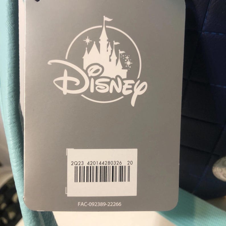 May include: A gray tag with the Disney logo, featuring a castle silhouette. Below the logo is a barcode and the text "2Q23 420144280326 20" and "FAC-092389-22266". The tag is attached to a blue item.