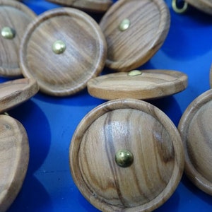 May include: A group of round wooden buttons with a brass center. The buttons have a natural wood grain pattern and are arranged on a blue surface.