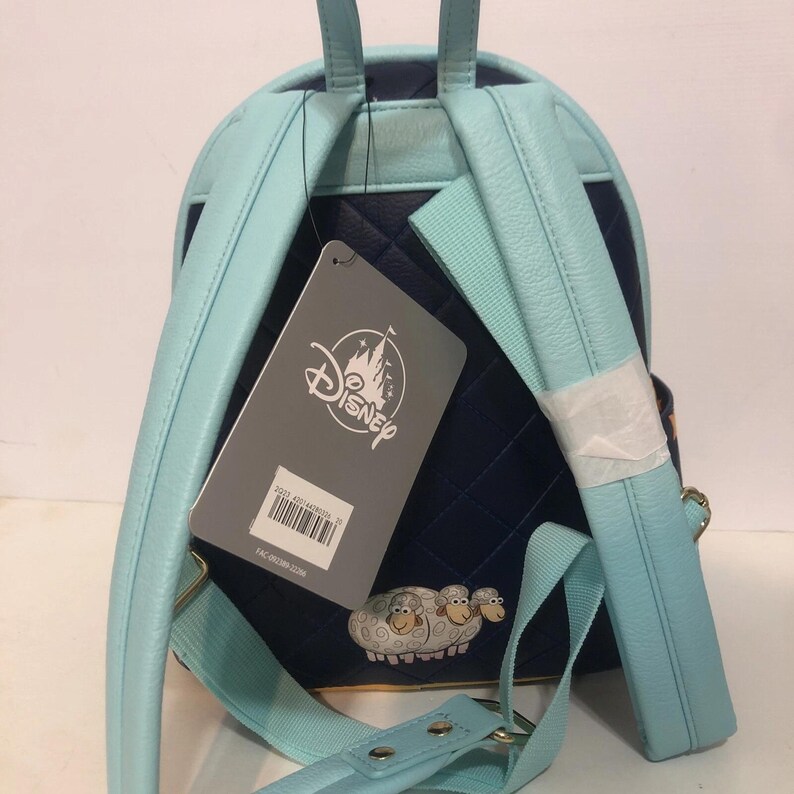 May include: A light blue and navy blue Disney backpack with a quilted pattern. The backpack features light blue straps and a Disney tag. A graphic of three sheep is on the bottom of the backpack.