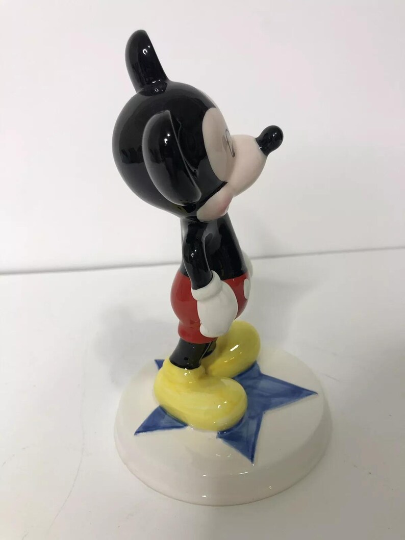 Op de afbeelding: Een keramiek beeldje van Mickey Mouse dat op een blauwe ster staat. Mickey draagt zijn kenmerkende rode broek, gele schoenen en witte handschoenen. Hij kijkt naar rechts.