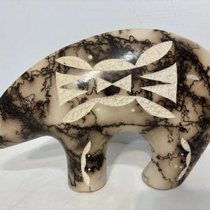 May include: A bear-shaped ceramic sculpture featuring a cream-colored base with intricate black horsehair-style markings. The surface is adorned with inlaid white textured geometric shapes on the side and legs, creating a distinct contrast.