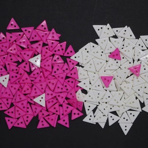 May include: A large pile of pink triangle buttons with a smaller pile of white triangle buttons. Both piles are arranged in a heart shape.