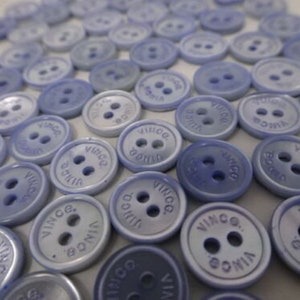 May include: A large collection of light blue plastic buttons with the word "VINCE." printed on each button.