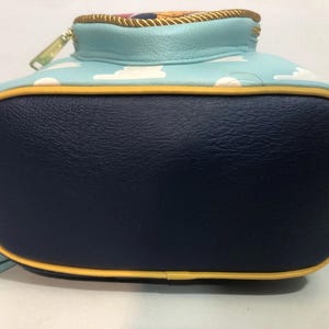 May include: A backpack with a navy blue base, light blue top, and yellow trim. The top features a sky blue pattern with white clouds. The zipper is gold. The backpack has light blue straps.