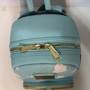 May include: A light blue backpack with gold zippers and a cloud pattern on the bottom. The backpack has a small top handle and adjustable straps. The zippers have the words "Disney Parks" and "Loungefly" on them.