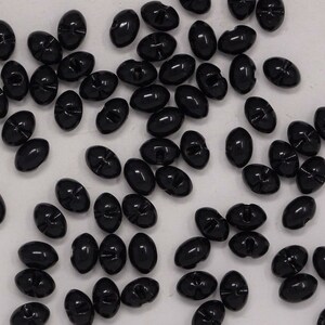May include: A large collection of black oval buttons with two holes. The buttons are scattered on a white surface.