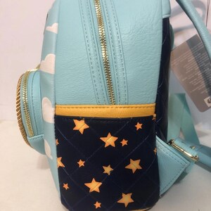 May include: A light blue backpack with white cloud designs and gold zippers. The side pocket is navy blue with a quilted pattern and gold stars. The backpack has a yellow trim.